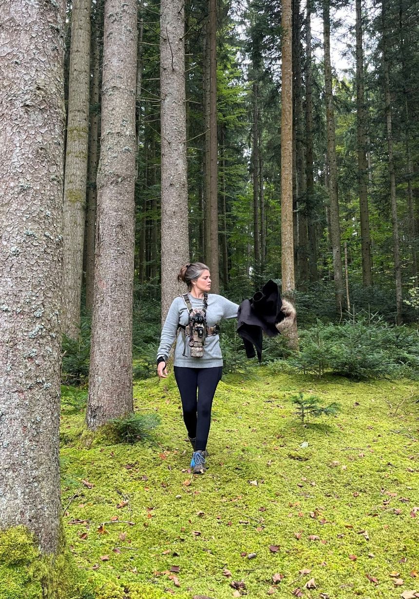 Alice Sinclair walking with her camera through a pine forest